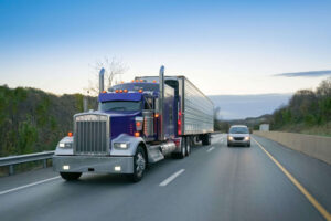 Image of a semi tractor trailer on the highway driving beside a small car, representing how The Law Office of M. Andrew Brison can help defend against West Virginia trucking accident claims.